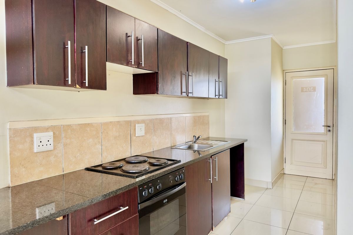 A functional kitchen featuring dark wood cabinetry, granite countertops, a built-in electric hob and oven, and neutral tiled flooring.