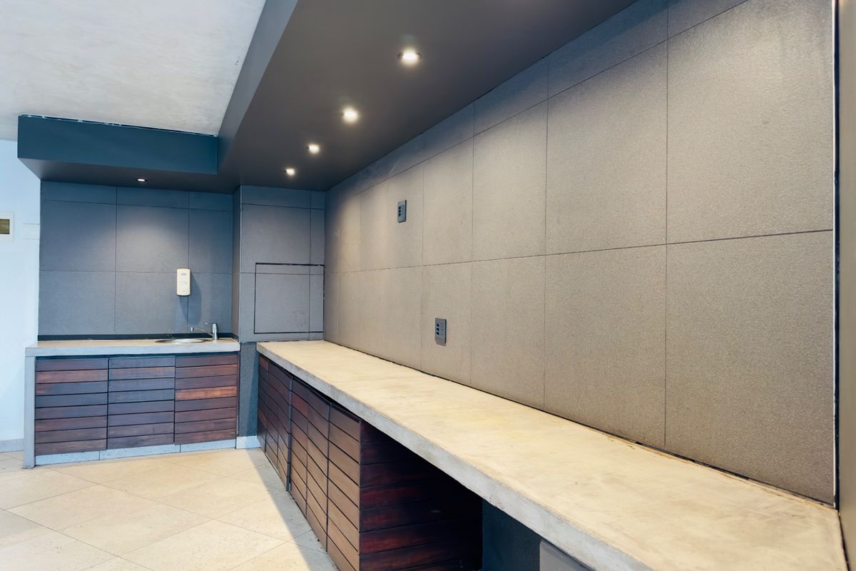 A modern, minimalist kitchen area featuring concrete countertops, timber cabinetry, and large-format wall tiling with integrated recessed lighting.