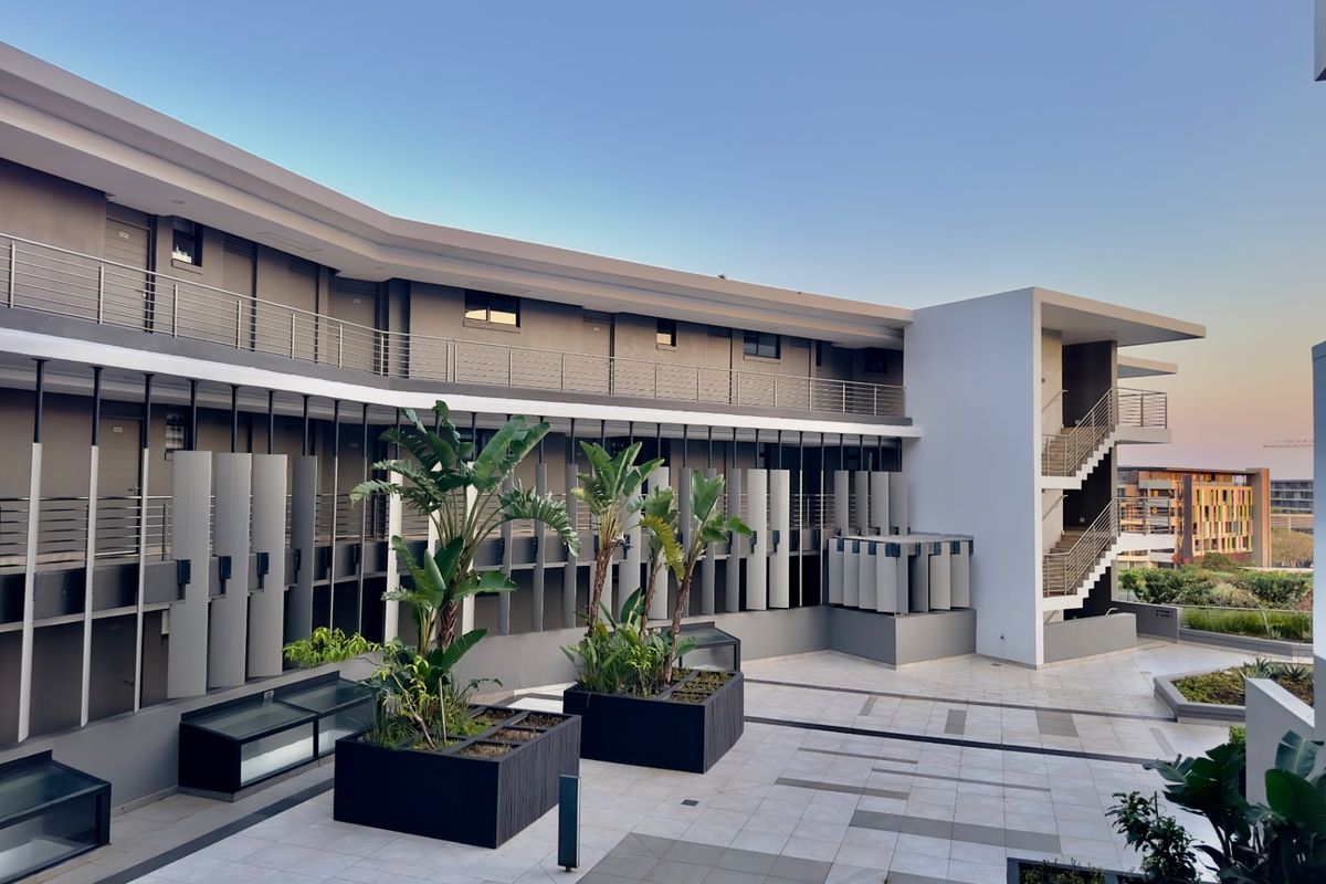 Modern apartment complex exterior featuring a paved courtyard, architectural staircase, metal railings, and integrated planters.