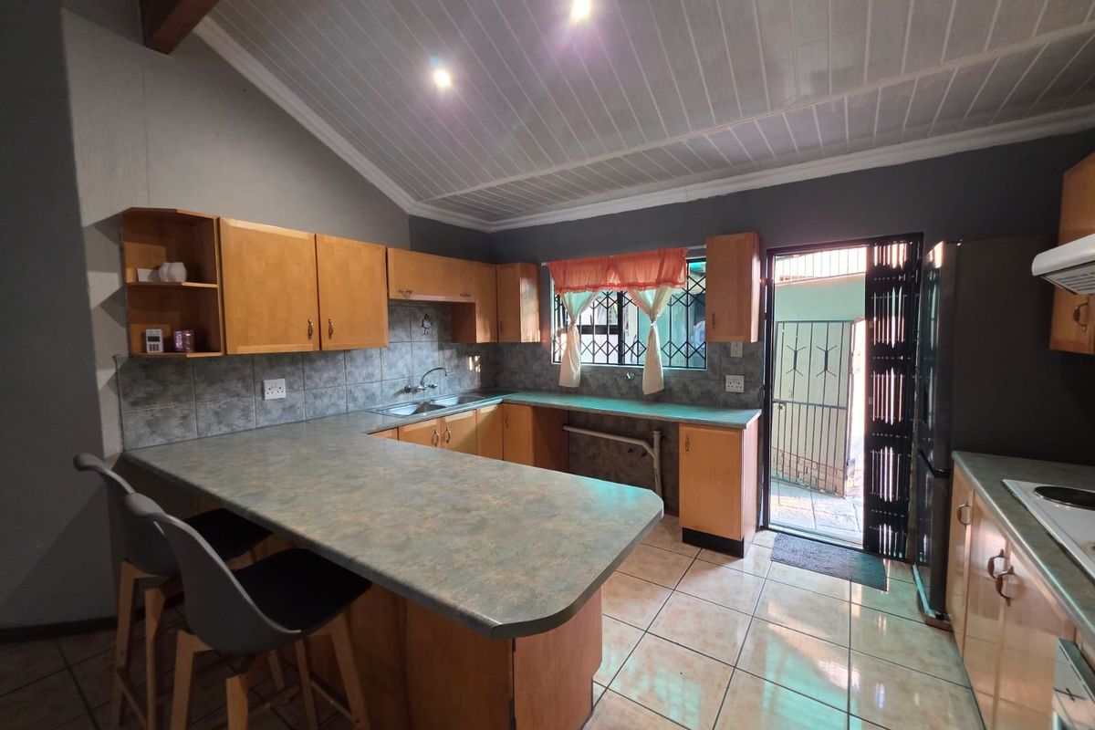 A functional kitchen featuring laminate cabinetry, tiled backsplash, and a breakfast bar, with direct access to an exterior area through a security gate.