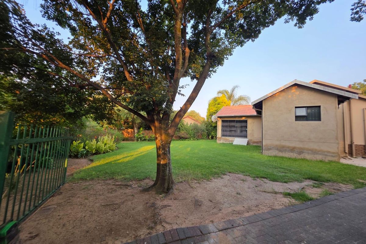 A spacious rear garden featuring a well-maintained lawn, mature tree, and paved access, adjacent to the rear elevation of the house.