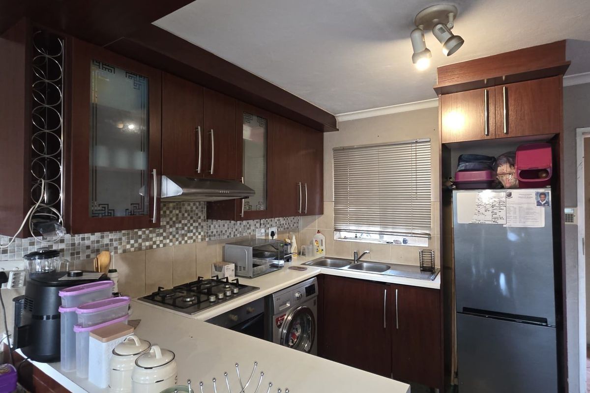 A functional kitchen featuring dark wood cabinetry, a gas hob with extractor, mosaic tile backsplash, and a built-in washing machine.
