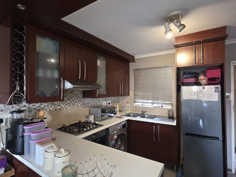 A functional kitchen featuring dark wood cabinetry, a gas hob with extractor, mosaic tile backsplash, and a built-in washing machine.