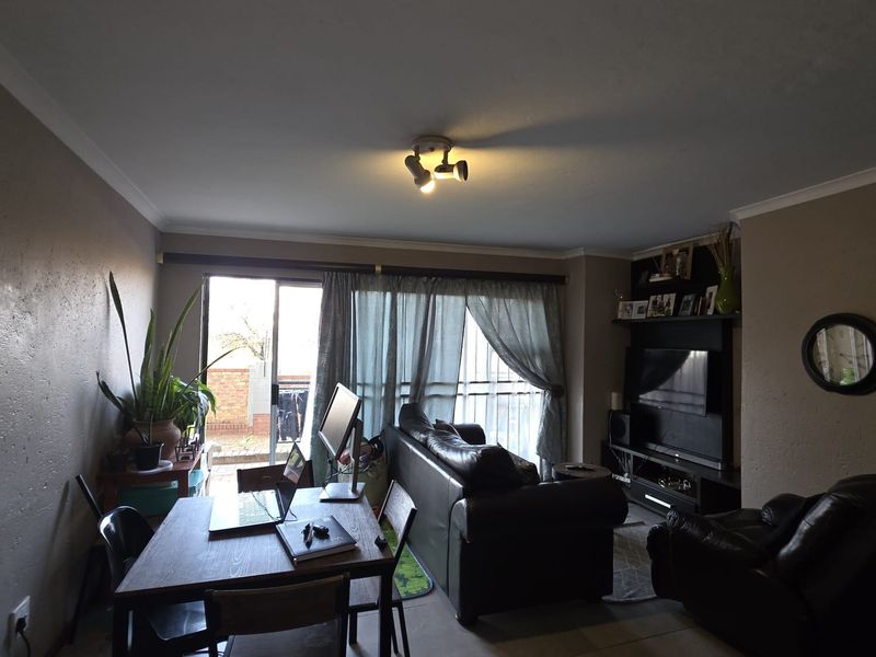Open-plan living and dining area featuring tiled flooring, cove cornicing, and a built-in media unit with direct access to an outdoor patio area.
