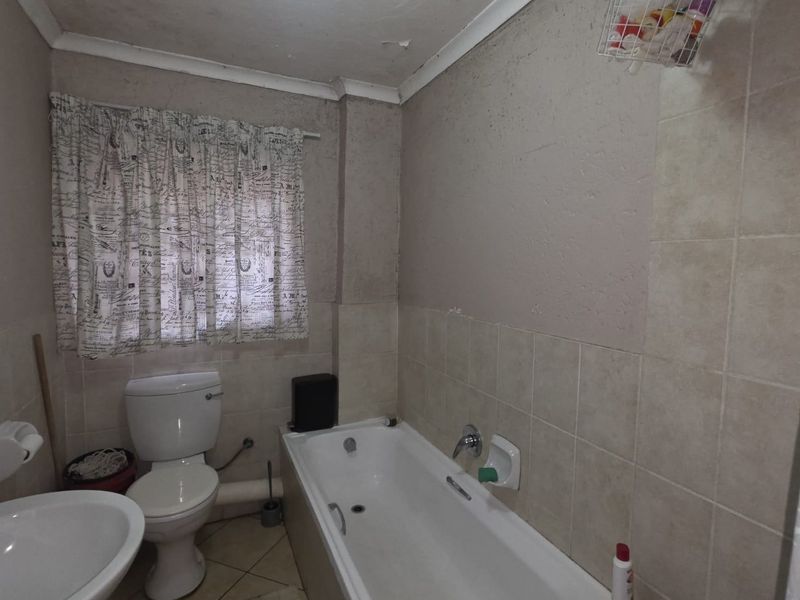 A functional bathroom featuring a bathtub, pedestal basin, and toilet, with tiled finishes. The space requires cosmetic updates to the ceiling and wall surfaces.