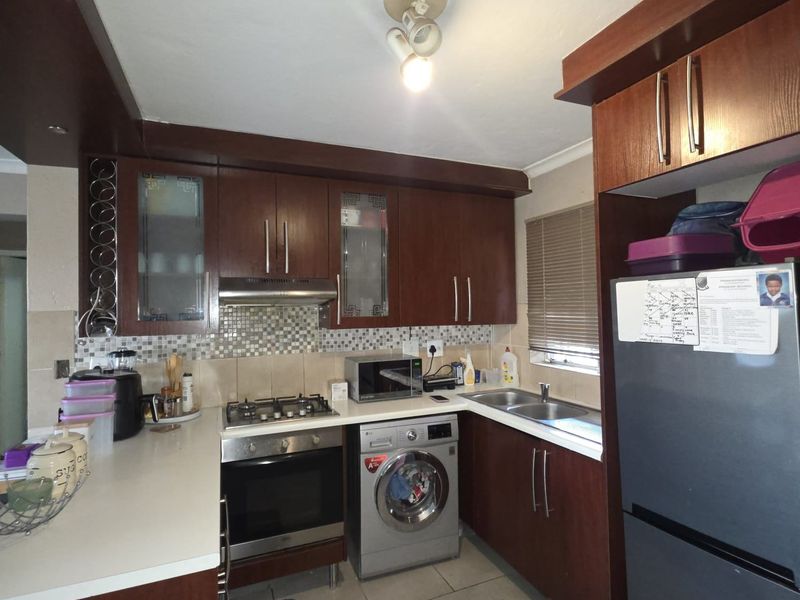 A functional kitchen featuring dark wood cabinetry, a gas hob with extractor, built-in oven, double sink, and tiled backsplash with neutral floor tiles.