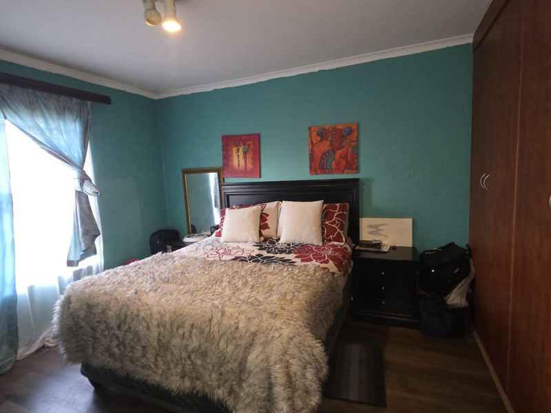 A bedroom featuring laminate flooring, a built-in wardrobe, and a ceiling light fixture, with teal-painted walls.