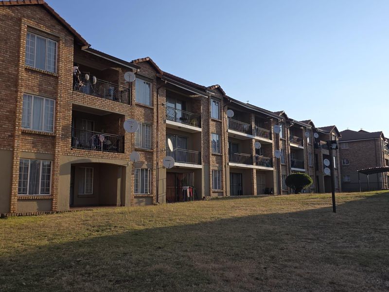 Rear view of a multi-story apartment complex featuring face brick construction, private balconies, and a shared lawn area.