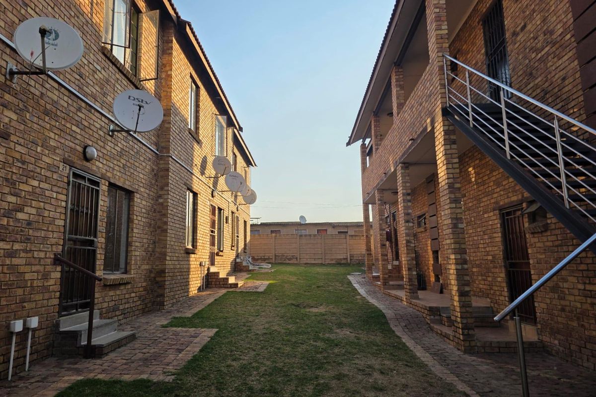 Exterior view of an apartment complex featuring face brick buildings, paved walkways, a central lawn area, and external staircases.