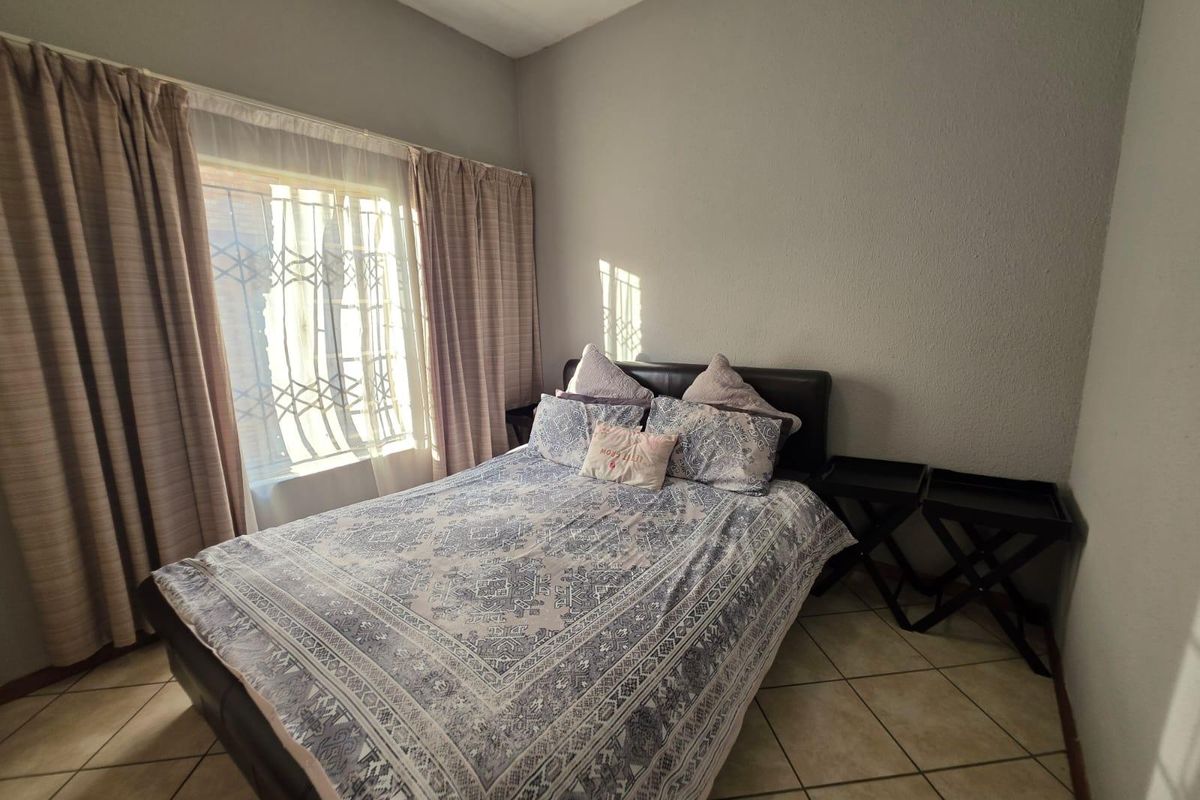 A functional bedroom featuring tiled flooring and a window fitted with a security gate, providing natural light and basic security.