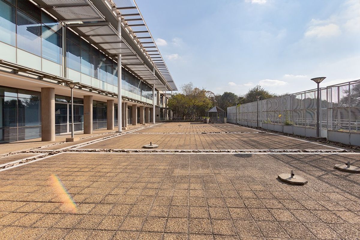 Spacious paved outdoor terrace area featuring modern glass facade architecture, metal shading structures, and perimeter security fencing.