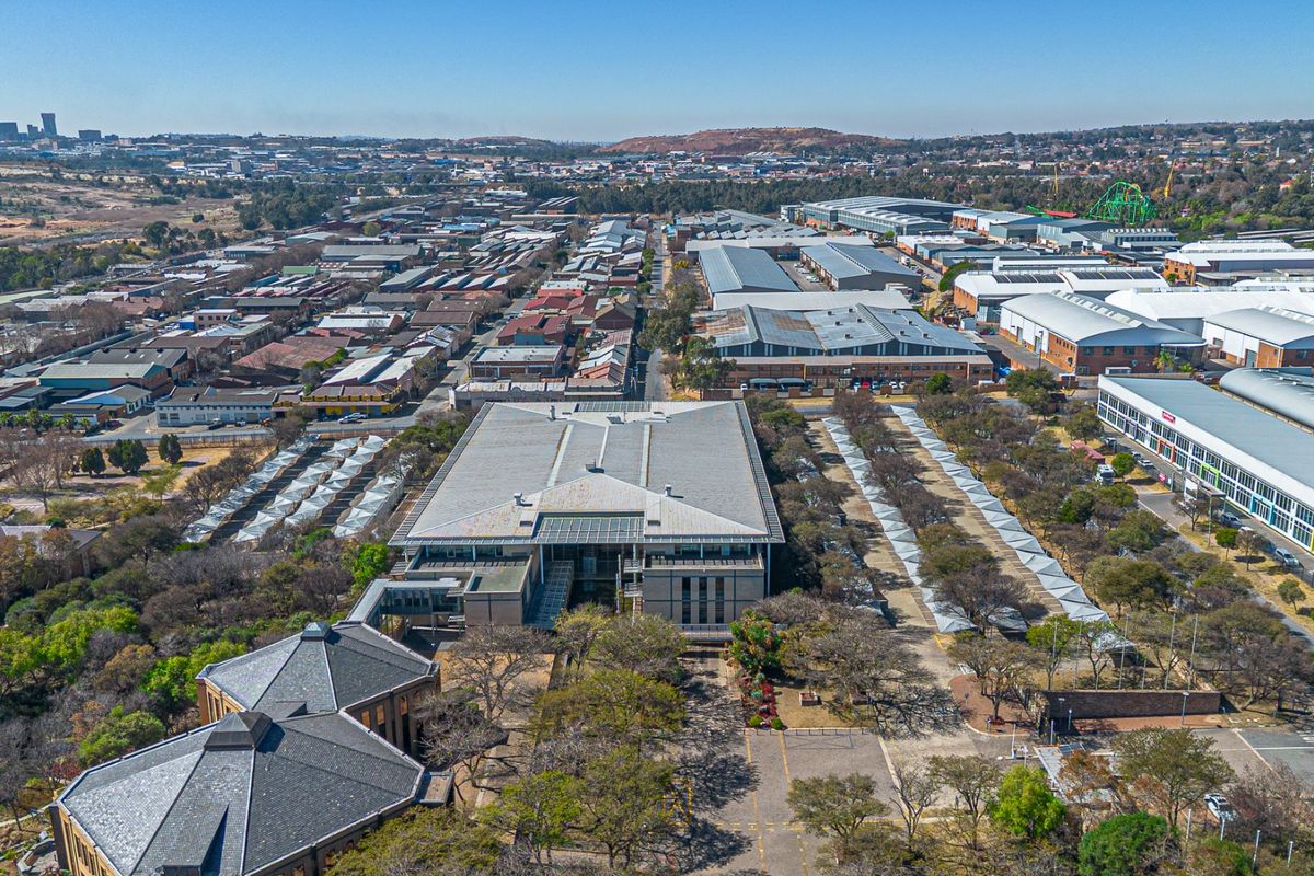 An aerial view of a commercial property complex featuring multiple buildings, extensive parking facilities, and surrounding industrial and urban infrastructure.