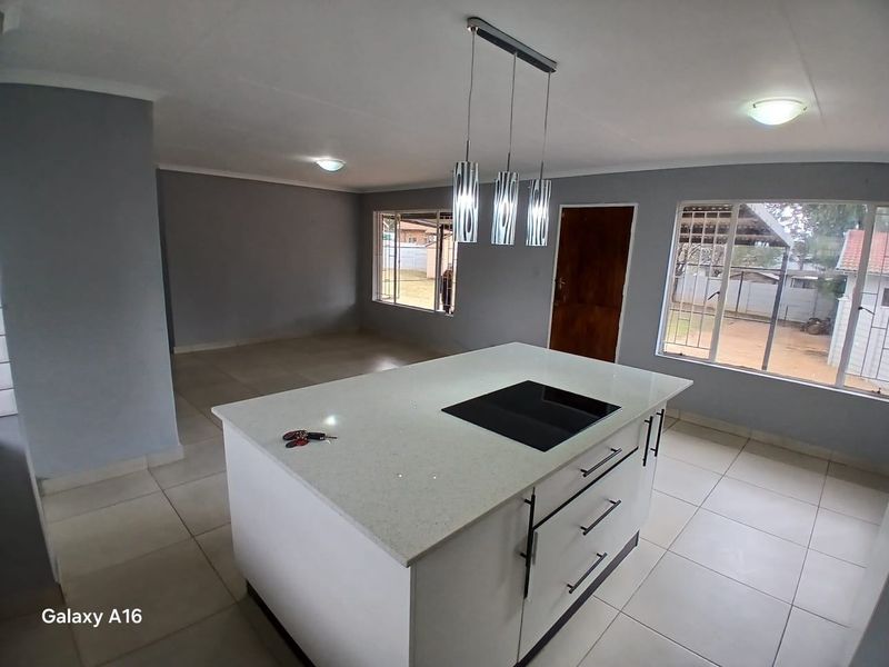 Open-plan living and kitchen area featuring a modern central island with a built-in induction hob, tiled flooring, and neutral grey walls.