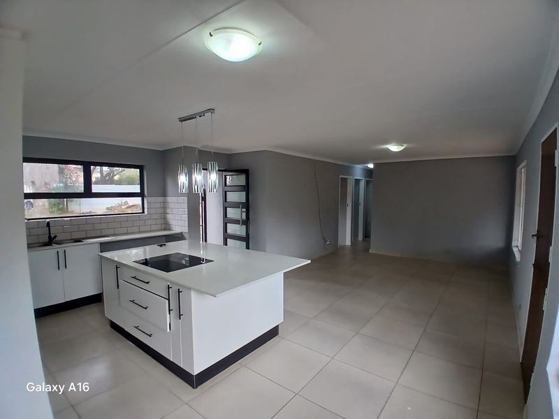 Spacious open-plan living area featuring a modern kitchen with a central island, built-in hob, and neutral tiled flooring throughout.