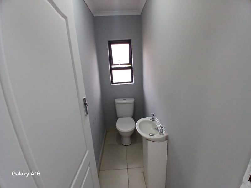 A clean and functional guest bathroom featuring a pedestal basin, toilet, and neutral tiled flooring.