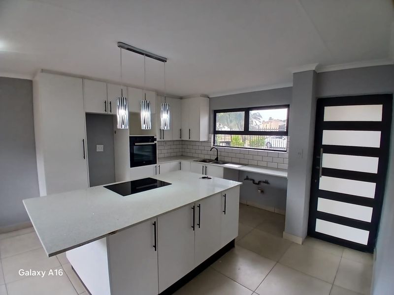 Modern kitchen featuring a central island with an integrated hob, built-in oven, subway tile backsplash, and sleek white cabinetry.