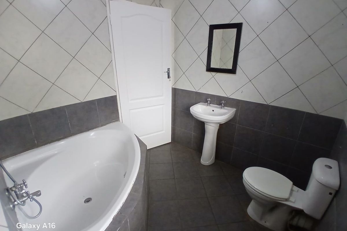 A functional bathroom featuring a corner bathtub, pedestal basin, and toilet with contrasting grey and white tiled finishes.