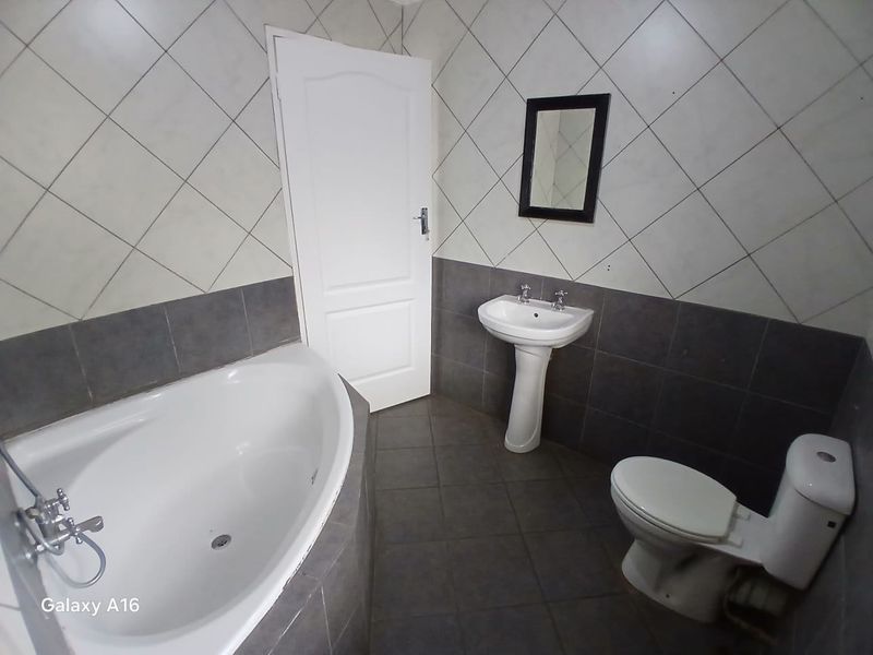 A functional bathroom featuring a corner bathtub, pedestal basin, and toilet with contrasting grey and white tiled finishes.