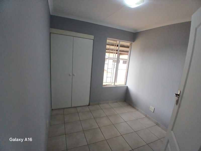 A clean, empty bedroom featuring tiled flooring, a built-in wardrobe, and a window fitted with security bars.