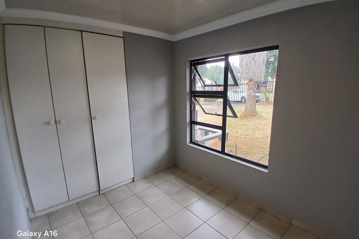 A clean, empty bedroom featuring neutral grey walls, tiled flooring, and a built-in wardrobe with ample storage space.