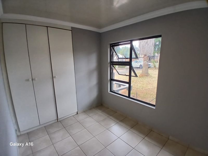 A clean, empty bedroom featuring neutral grey walls, tiled flooring, and a built-in wardrobe with ample storage space.