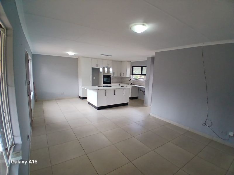 An open-plan living and kitchen area featuring a modern white kitchen island, built-in oven, and neutral tiled flooring throughout.
