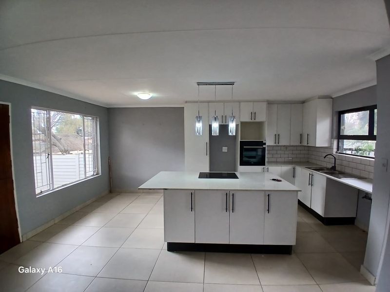 Modern open-plan kitchen featuring a central island with integrated cooktop, white cabinetry, subway tile backsplash, and contemporary pendant lighting.