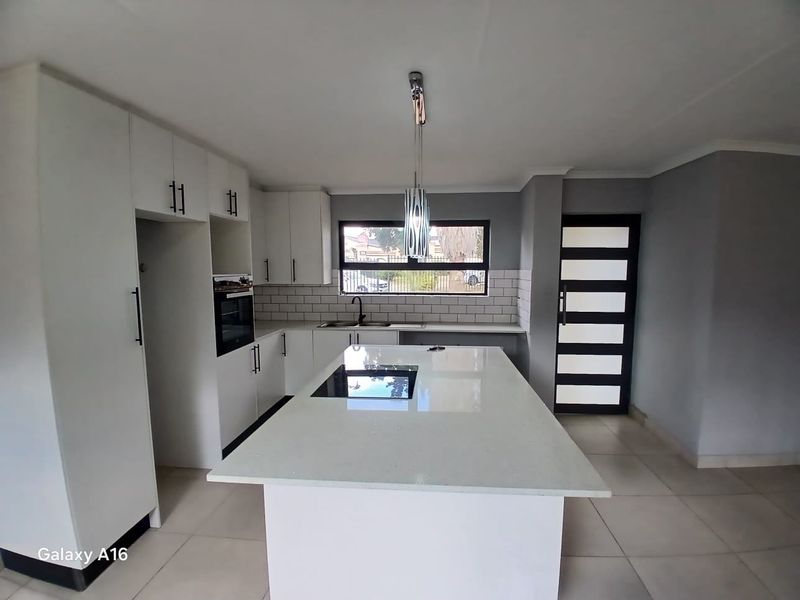 Modern kitchen featuring a central island with a built-in hob, white cabinetry, subway tile backsplash, and sleek finishes throughout.