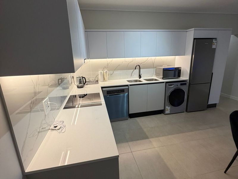 Modern kitchen featuring sleek handleless cabinetry, quartz countertops, marble-look splashback, integrated hob, and high-quality tiled flooring with contemporary track lighting.