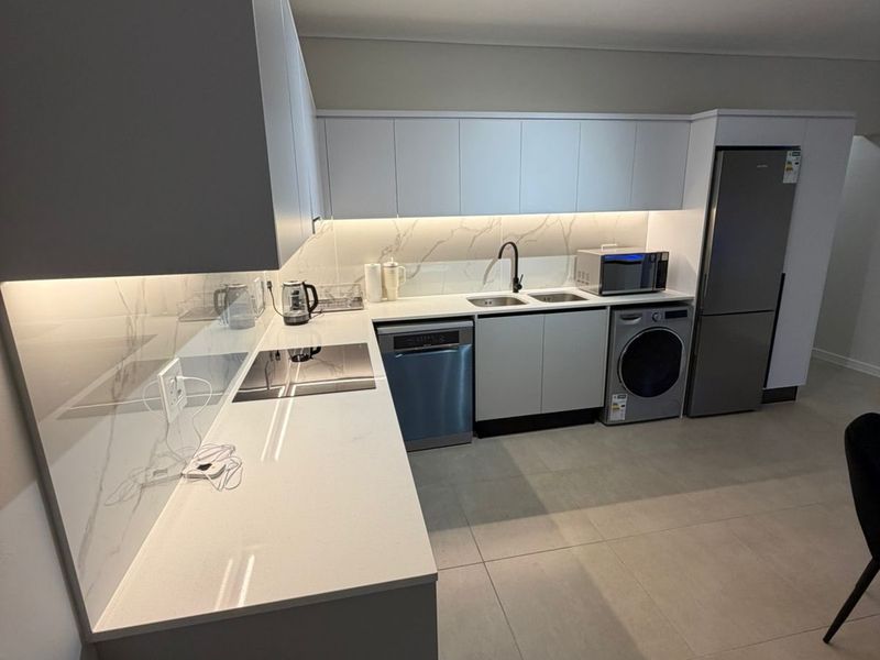 Modern kitchen featuring sleek white cabinetry, quartz countertops, marble-look splashback, integrated appliances, and contemporary track lighting.