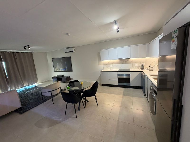 Modern open-plan living area featuring a sleek kitchen with built-in appliances, marble-look splashback, and tiled flooring, seamlessly flowing into the lounge space.