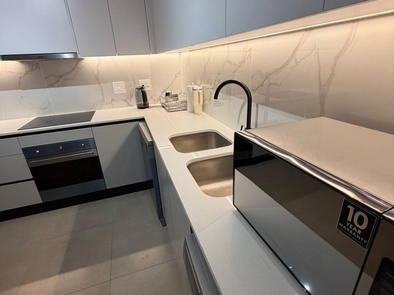 Modern kitchen featuring sleek handleless cabinetry, stone countertops, marble-look splashback, integrated appliances, and high-quality finishes throughout.