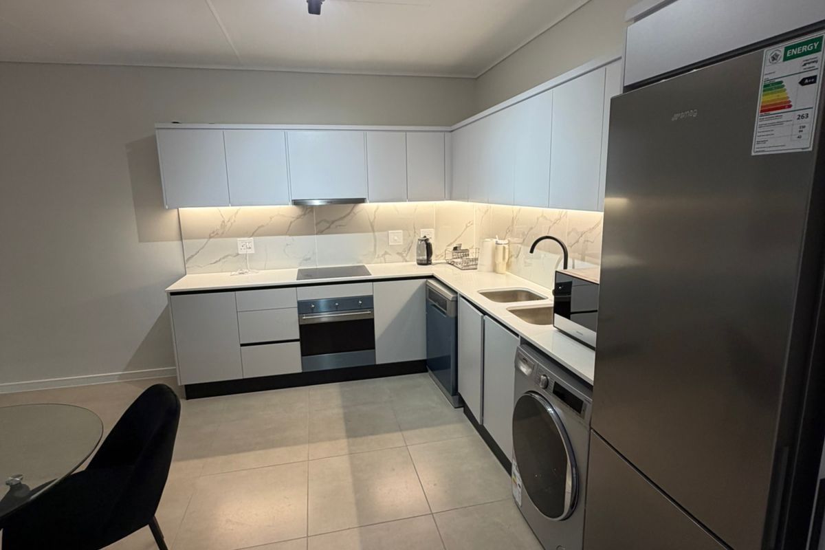Modern kitchen featuring sleek white cabinetry, marble-look backsplash, stone countertops, and integrated appliances including an oven, hob, and extractor fan.