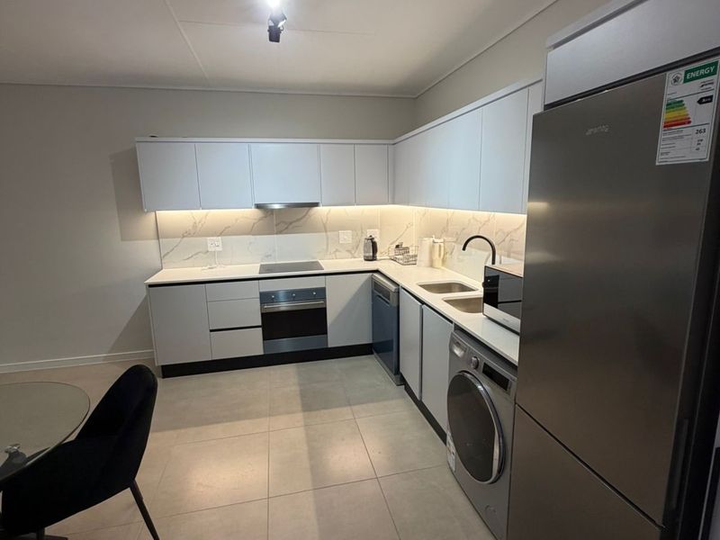 Modern kitchen featuring sleek white cabinetry, marble-look backsplash, stone countertops, and integrated appliances including an oven, hob, and extractor fan.