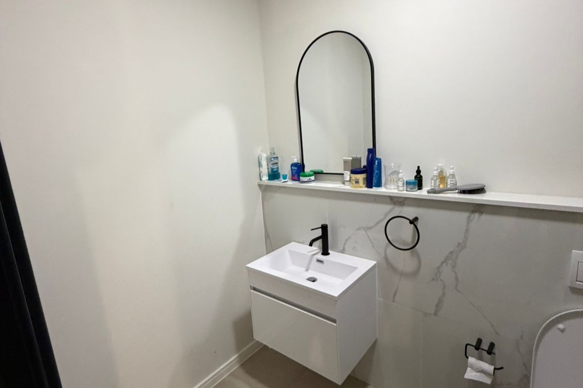 A modern bathroom featuring a wall-mounted vanity with a black mixer tap, an arched mirror, and marble-look tiled splashback.
