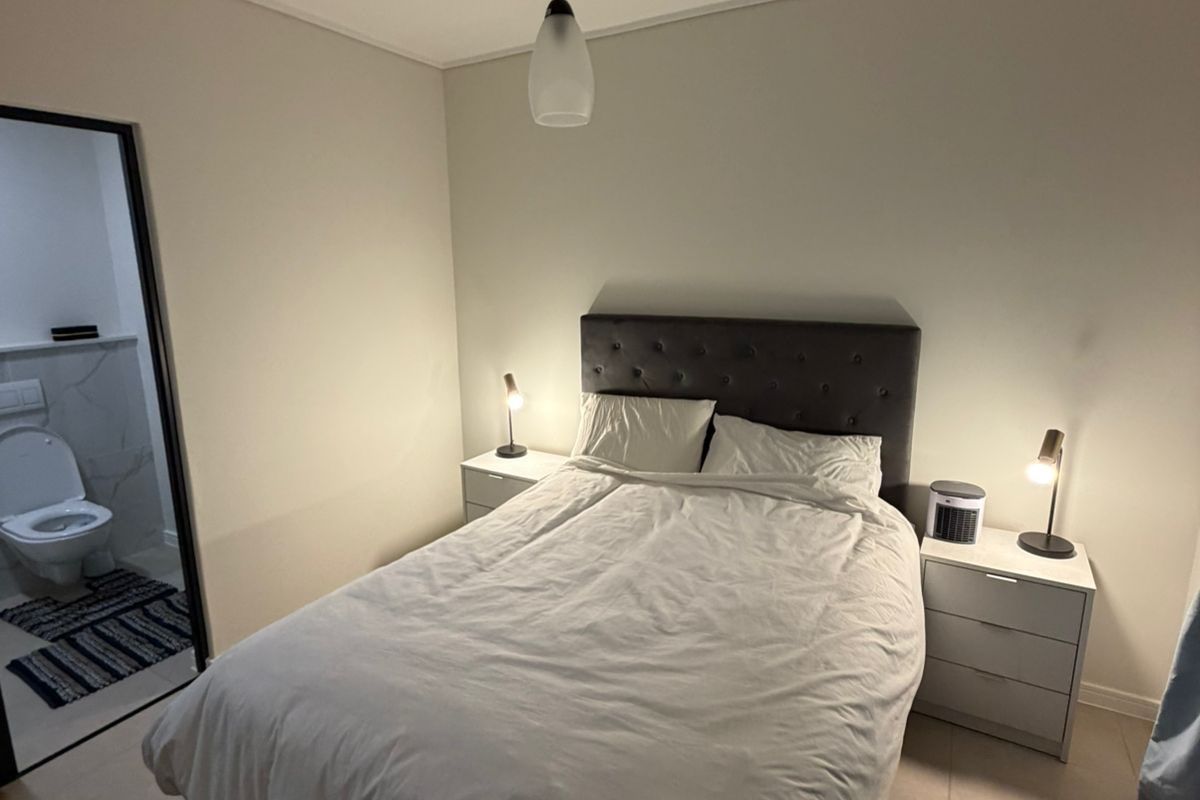 A well-maintained bedroom featuring neutral tiled flooring, a central pendant light, and direct access to an en-suite bathroom.