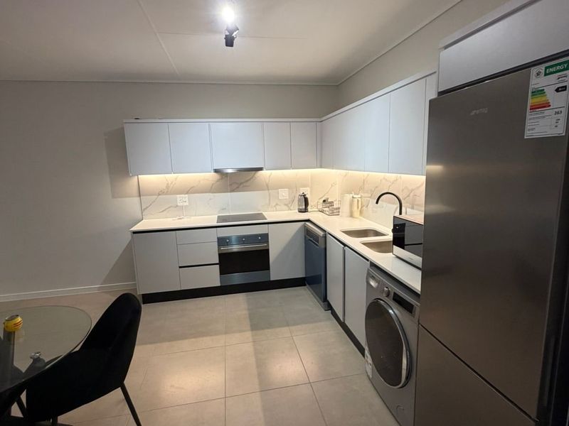 Modern kitchen featuring sleek white cabinetry, stone-look backsplash, integrated oven, electric hob, and high-quality tiled flooring in a clean, contemporary layout.