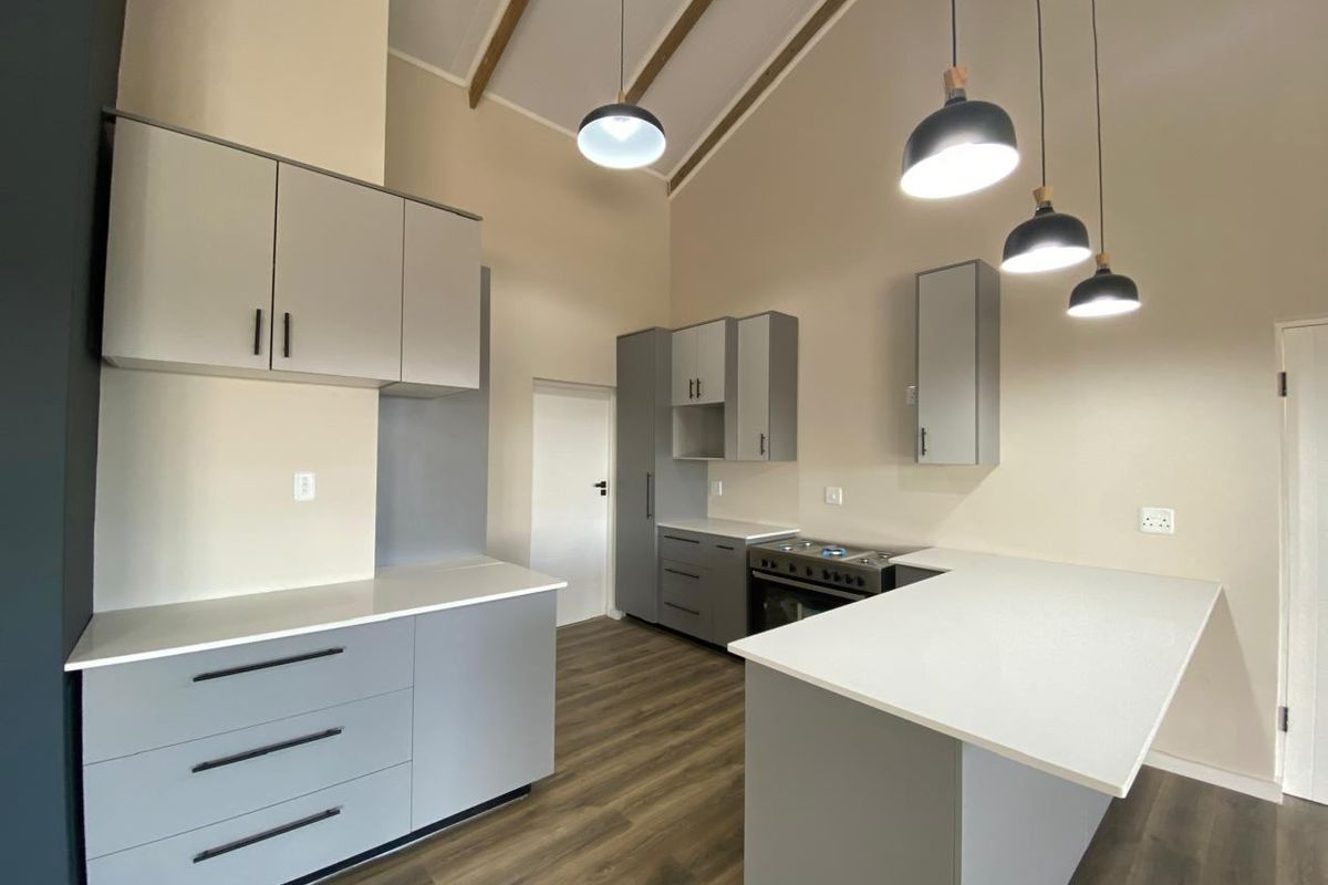 Modern kitchen featuring light grey cabinetry, stone countertops, a freestanding stove, and a high vaulted ceiling with exposed beams and contemporary pendant lighting.