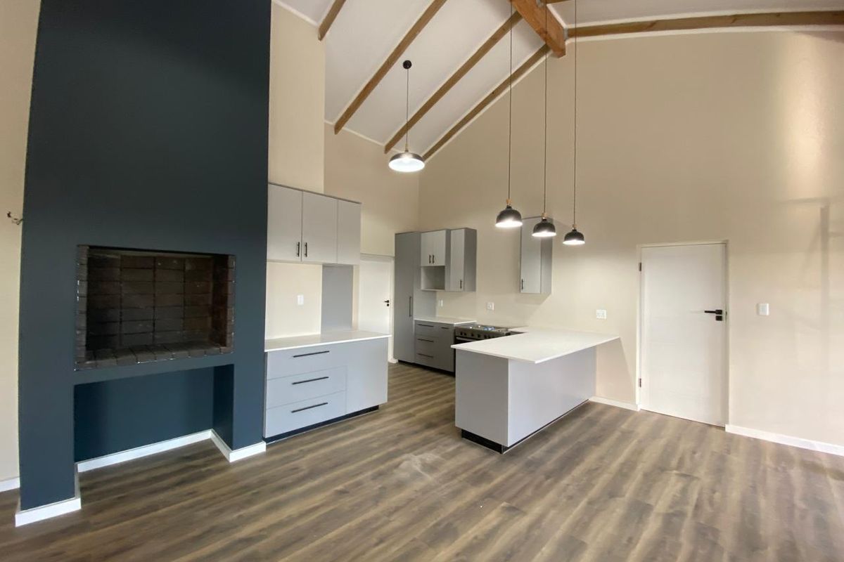 Spacious open-plan living area featuring a modern kitchen with island, exposed timber beams, and a striking dark-accented built-in fireplace.