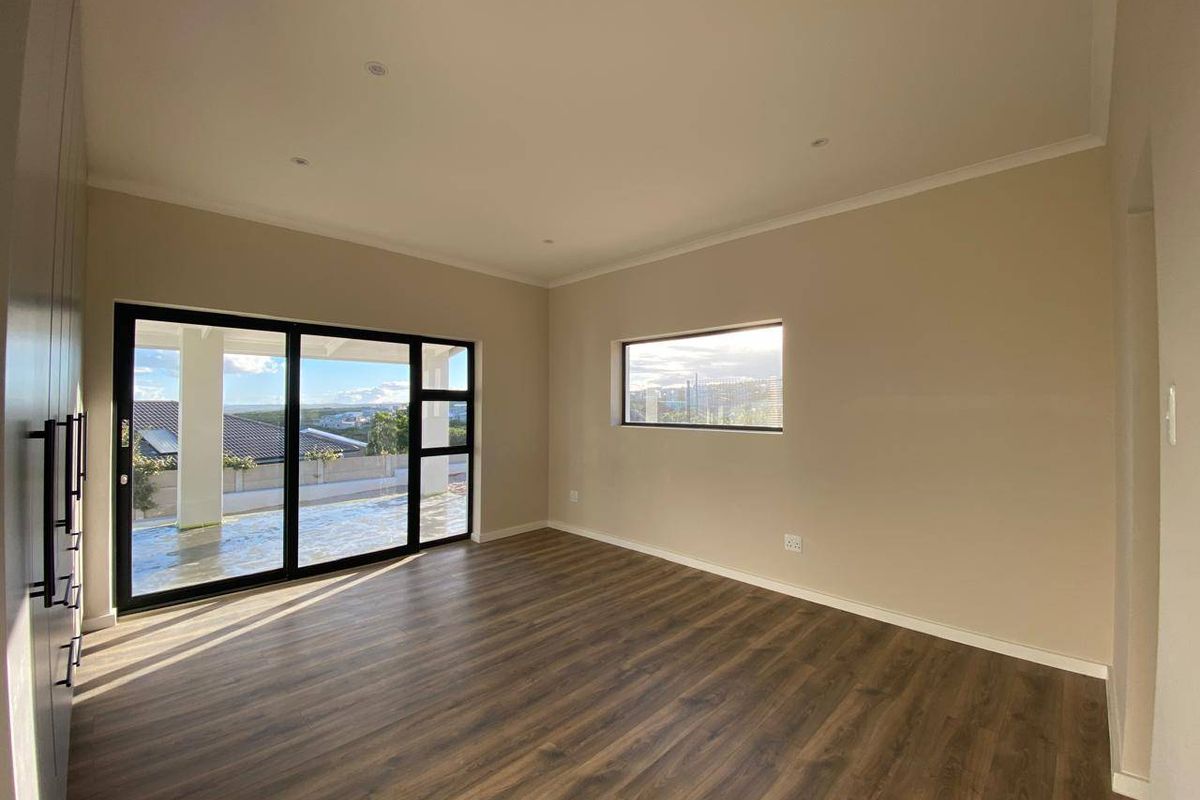 A bright, modern bedroom featuring laminate flooring, built-in cupboards, and large sliding glass doors that open to an outdoor area.