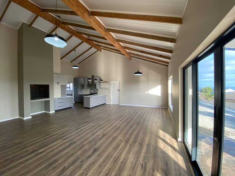 Spacious open-plan living area featuring vaulted ceilings with exposed timber beams, a built-in fireplace, modern kitchen cabinetry, and large sliding doors leading outdoors.
