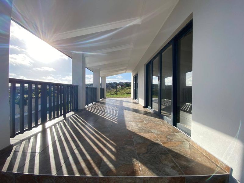 A spacious covered patio featuring tiled flooring, modern sliding glass doors, and a secure railing, offering a bright outdoor living space.