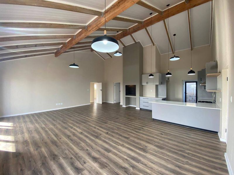 Spacious open-plan living and kitchen area featuring vaulted ceilings with exposed timber beams, modern cabinetry, a built-in fireplace, and durable laminate flooring.