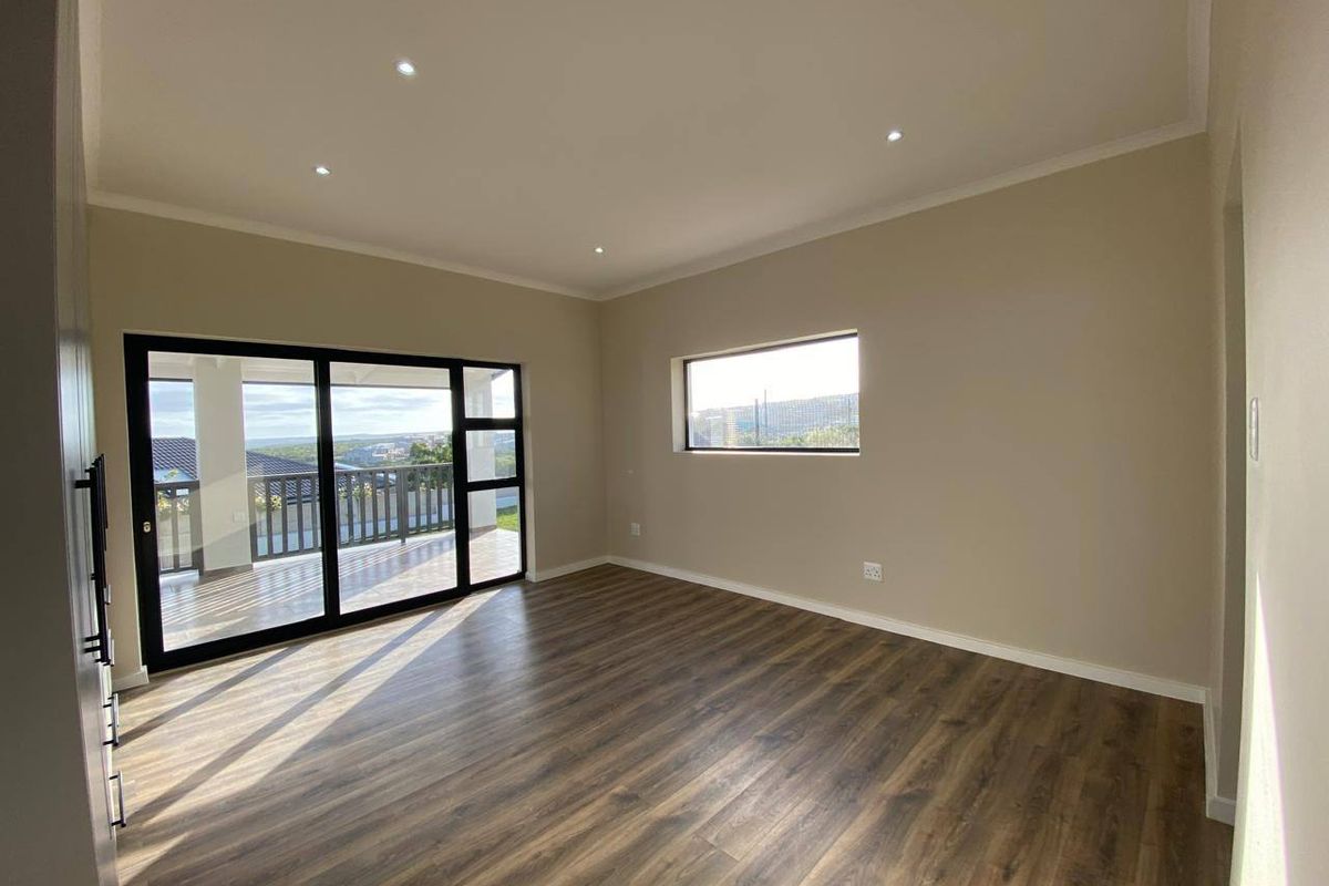 A bright, empty living room featuring modern laminate flooring, recessed downlights, and large black aluminium sliding doors leading to an outdoor balcony.