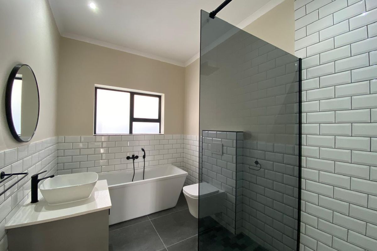 Modern bathroom featuring a freestanding bathtub, wall-mounted toilet, glass shower screen, and contemporary black tapware with subway tile finishes.