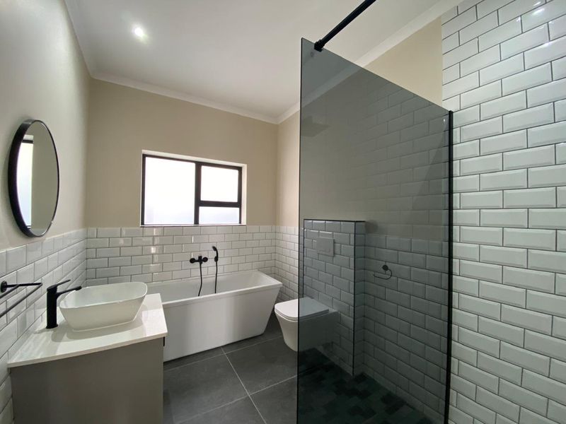 Modern bathroom featuring a freestanding bathtub, wall-mounted toilet, glass shower screen, and contemporary black tapware with subway tile finishes.