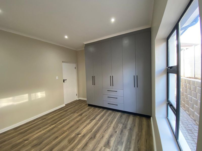A bright, modern bedroom featuring sleek grey built-in cupboards, durable laminate flooring, and large windows allowing for ample natural light.