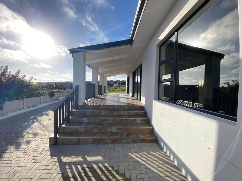 A spacious covered patio featuring tiled steps, metal railings, and direct access to the paved driveway and surrounding outdoor area.