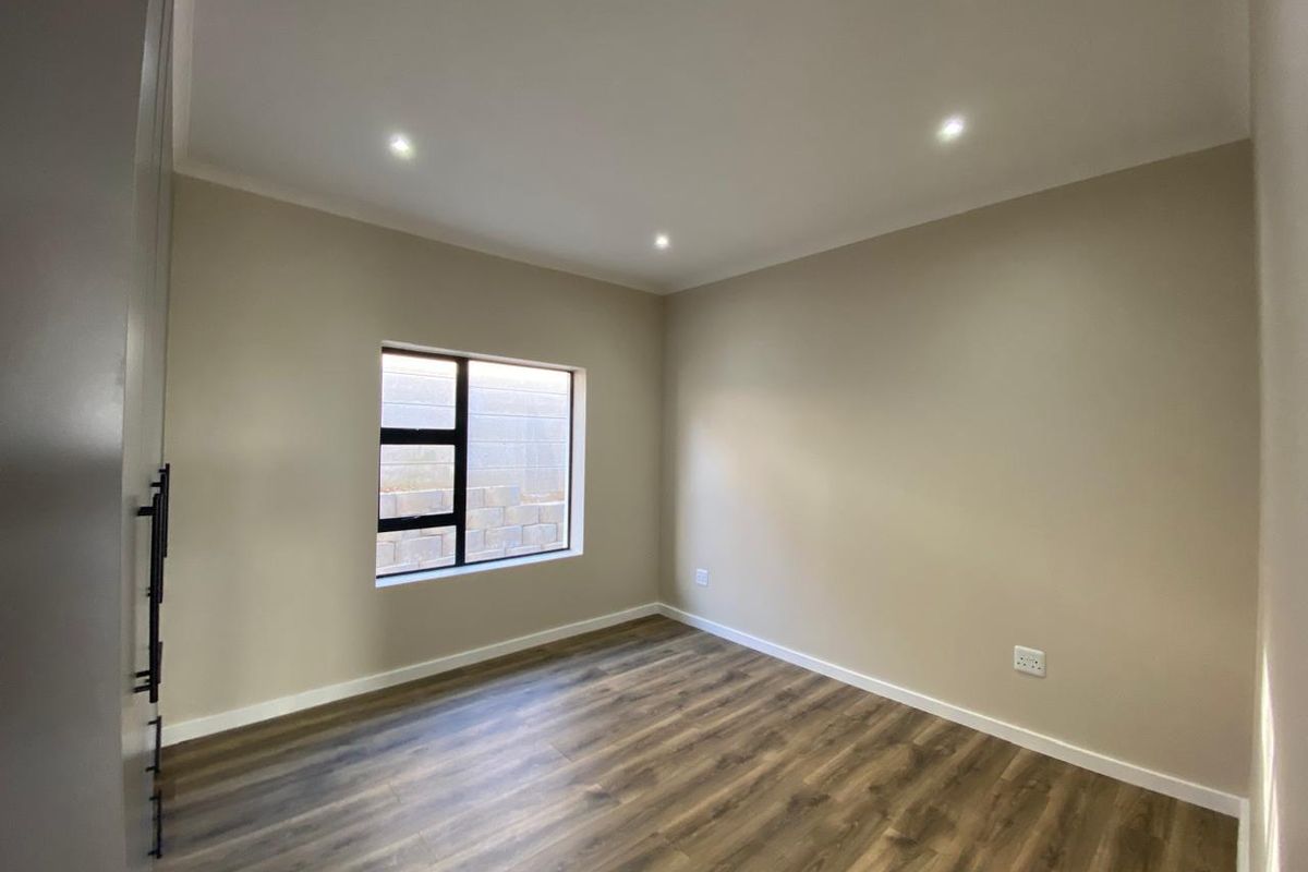 A clean, modern bedroom featuring neutral walls, durable laminate flooring, recessed downlights, and built-in cupboards, offering a versatile space ready for furnishing.