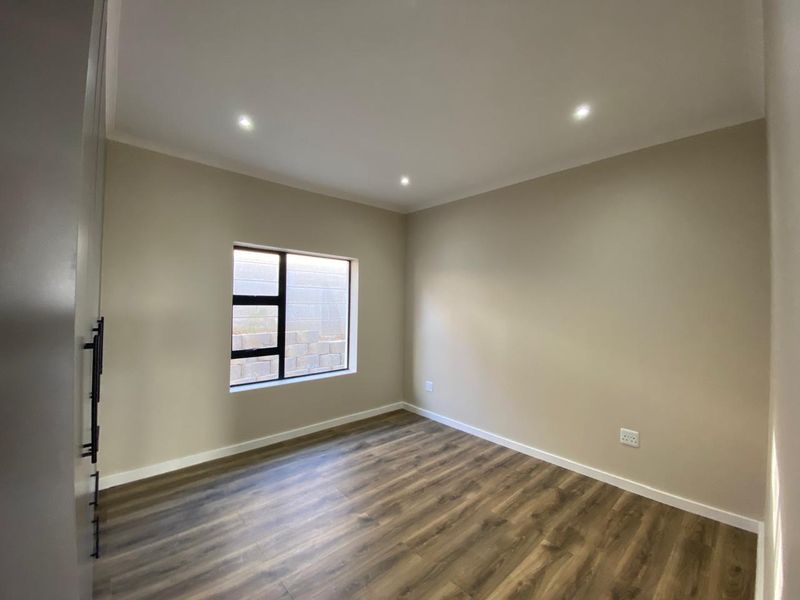 A clean, modern bedroom featuring neutral walls, durable laminate flooring, recessed downlights, and built-in cupboards, offering a versatile space ready for furnishing.